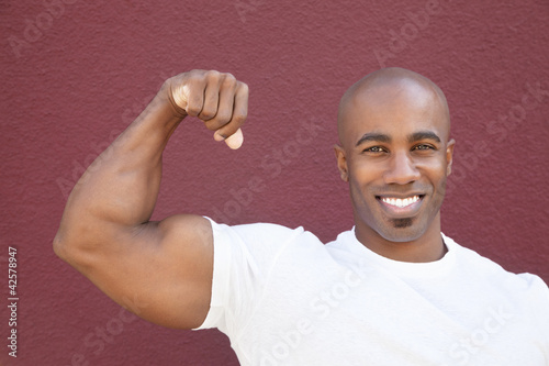 Photo: Portrait of a young African American man flexing muscles over colored background Portrait of a young African American man flexing muscles over colored background