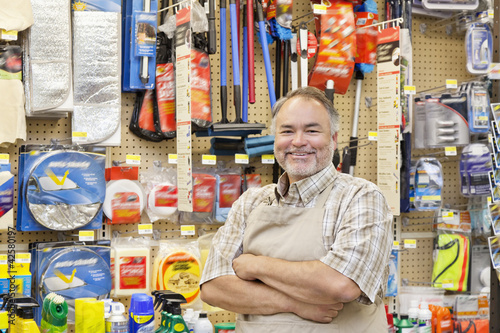 Photo: Portrait of a happy mature salesperson with arms crossed in hardware store Portrait of a happy mature salesperson with arms crossed in hardware store