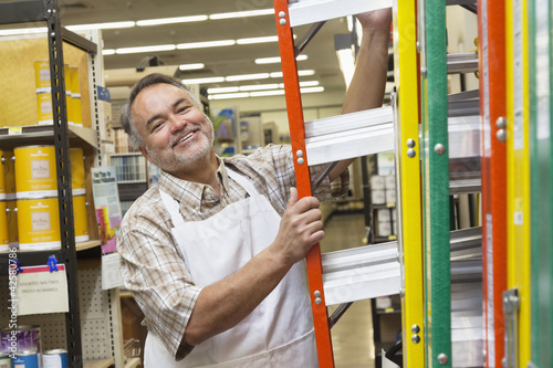 Photo: Portrait of a happy mature man with ladder in hardware store Portrait of a happy mature man with ladder in hardware store