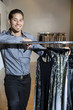 Foto: Portrait of a happy young male standing by clothes rack in fashion store Portrait of a happy young male standing by clothes rack in fashion store