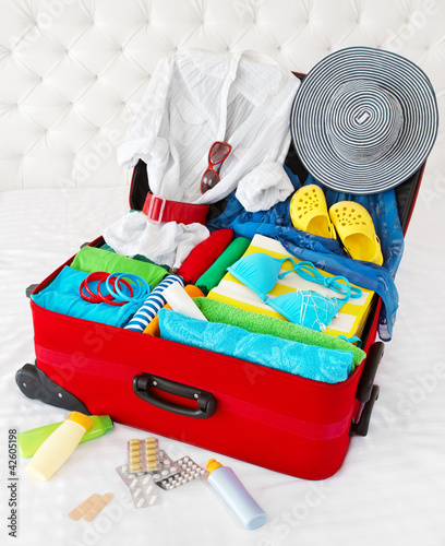 Photo: Red travel suitcase packed for vacation with personal belongings Red travel suitcase packed for vacation with personal belongings