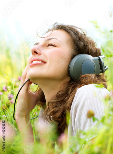 Photo: Beautiful Young Woman with Headphones Outdoors. Enjoy Music Beautiful Young Woman with Headphones Outdoors. Enjoy Music