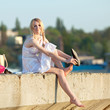 Attractive young woman in white sundress puts on shoes outdoors