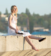Attractive young woman in white sundress puts on shoes outdoors