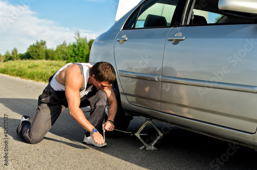 Photo: Mechanic lifting a car with jack-screw Mechanic lifting a car with jack-screw