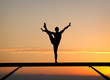 silhouette of female gymnast on balance beam in sunset