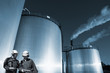 oil workers with storage towers in background, blue toning idea