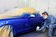 Worker painting a blue car.