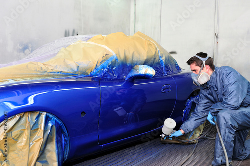 Photo: Worker painting a blue car. Worker painting a blue car.