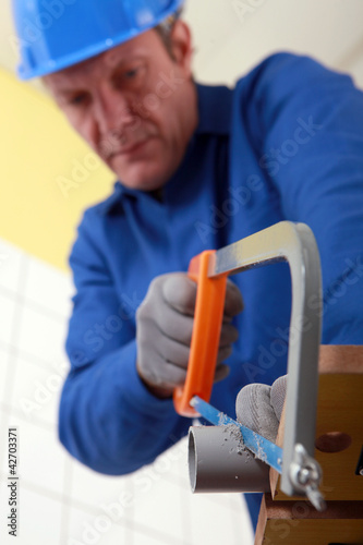 Photo: Tradesman cutting a tube with a saw Tradesman cutting a tube with a saw