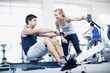 Personal trainer with man on rowing machine in gymnasium