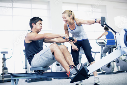Photo: Personal trainer with man on rowing machine in gymnasium Personal trainer with man on rowing machine in gymnasium