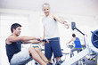 Personal trainer guiding man on rowing machine in gymnasium