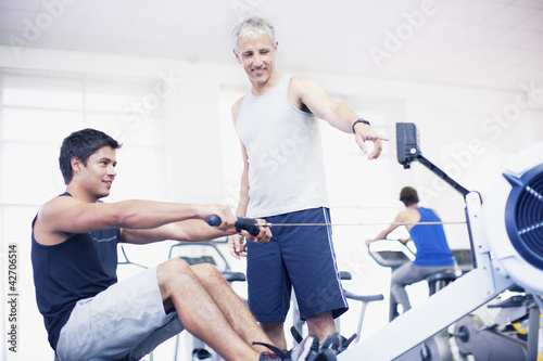 Photo: Personal trainer guiding man on rowing machine in gymnasium Personal trainer guiding man on rowing machine in gymnasium