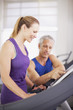 Man helping woman on treadmill in gymnasium