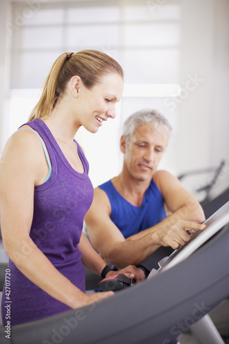 Photo: Man helping woman on treadmill in gymnasium Man helping woman on treadmill in gymnasium