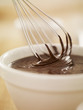 Close up of wire whisk dipping in bowl of melted chocolate