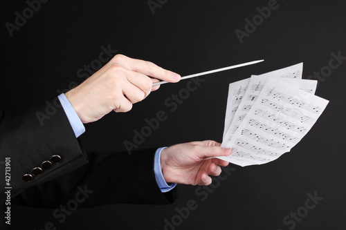 Photo: Music conductor hands with baton and notes isolated on black Music conductor hands with baton and notes isolated on black