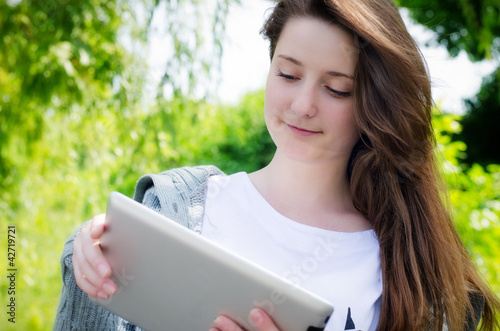 Photo: Young woman working on a tablet in the park Young woman working on a tablet in the park