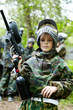 Boy in the camouflage suit holds a paintball gun barrel up