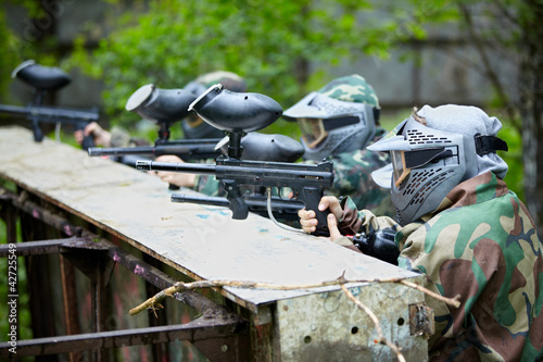 Foto: Four paintball players in camouflage and protective masks aims Four paintball players in camouflage and protective masks aims