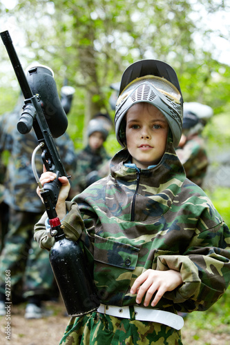 Photo: Boy in the camouflage suit holds a paintball gun barrel up Boy in the camouflage suit holds a paintball gun barrel up