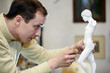 Sculptor works in studio on fragment of plaster sculpture.