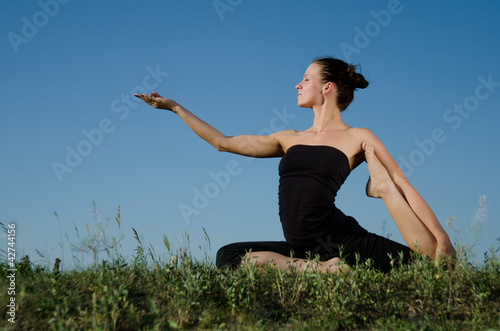 Photo: Yoga woman on green grass. Sky background. Yoga woman on green grass. Sky background.