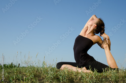 Photo: Yoga woman on green grass. Sky background. Yoga woman on green grass. Sky background.