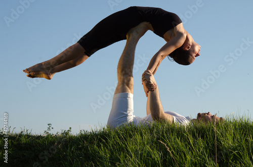 Photo: Two young man and woman couple doing yoga. Outdoors. Two young man and woman couple doing yoga. Outdoors.