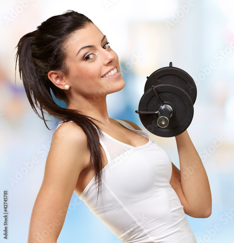 Photo: portrait of a young pretty woman holding weights and doing fitne portrait of a young pretty woman holding weights and doing fitne