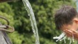 Boy refreshing his face in stream of water. Slow Motion.