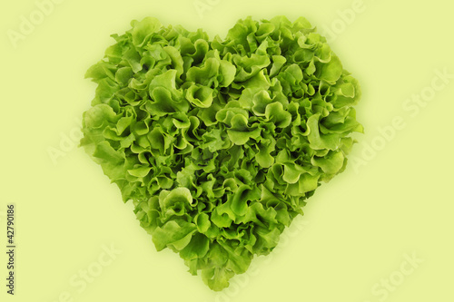 Photo: heart-shaped salad, lettuce on green background heart-shaped salad, lettuce on green background