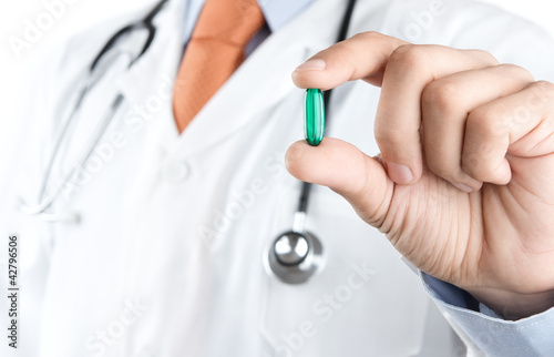 Photo: Close up of male doctor holding green pill Close up of male doctor holding green pill