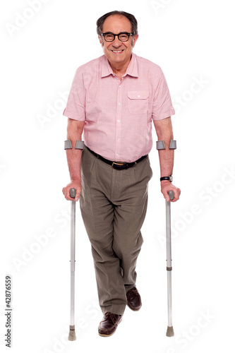 Photo: Smiling senior man walking with two crutches Smiling senior man walking with two crutches