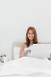 Woman sitting on her bed while using her credit card online
