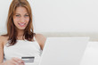 Attractive redheaded sitting on her bed while using her credit card online