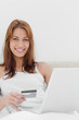 Portrait of a redheaded on her bed using her credit card online