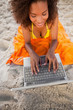 Young smiling woman using her laptop while lying on the beach