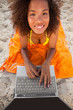 Young smiling woman looking up while using her laptop on her beach towel