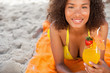 Young smiling woman lying on a beach towel while holding a fruit cocktail