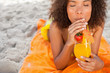 Young relaxed woman sipping a fruit cocktail while lying on the beach