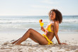 Side view of a young woman sitting on the beach while holding a cocktail