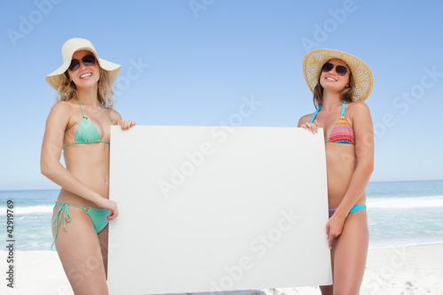 Photo: Two friends wearing sunglasses and hats while holding a blank poster Two friends wearing sunglasses and hats while holding a blank poster