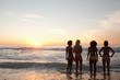 Four friends watching the sunset while standing near the waves