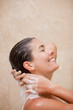 Side view of smiling woman washing her hair in the shower