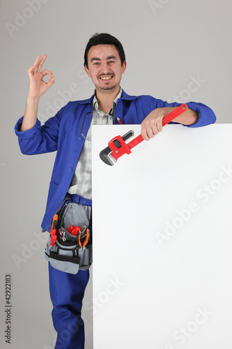 Photo: Tradesman giving the a-ok sign and standing behind a blank sign Tradesman giving the a-ok sign and standing behind a blank sign