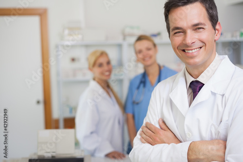 Photo: Pharmacist standing in a pharmacy with co-workers Pharmacist standing in a pharmacy with co-workers