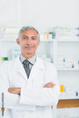 Photo: Pharmacist with his arms crossed standing in a pharmacy Pharmacist with his arms crossed standing in a pharmacy