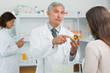 Pharmacist pointing at a flask of pills in front of a customer
